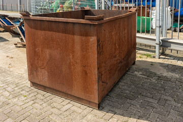 rusty rectangular brown metal bin stands outside on a factory site