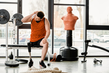 A disabled man with a prosthetic leg sitting on a bench in a gym, taking a moment to rest during...
