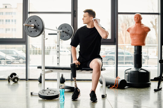 A disabled man with a prosthetic leg, sitting on a bench in a gym, taking a moment to rest during his workout session.