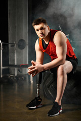 A man with a prosthetic leg sitting on top of a black tire in a gym, showcasing strength and...