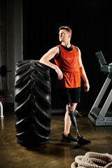 A disabled man with a prosthetic leg stands proudly next to a large tire in a gym, showcasing his...