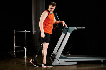 A disabled man with a prosthetic leg is standing on a treadmill in a dimly lit room, focused on his...