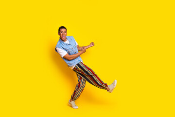 Fototapeta na wymiar Full size photo of optimistic man dressed denim vest print pants dancing on summer event isolated on vibrant yellow color background