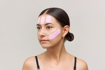 Young Caucasian pretty brunette woman with pink kinesio tape on her face to reduce wrinkles and...