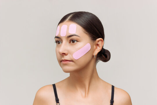 Young Caucasian pretty brunette woman with pink kinesio tape on her face to reduce wrinkles and tighten the oval of the face. Face care. Anti-aging effect.
