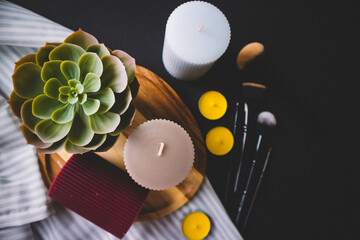 Candles, wooden board, makeup brushes, textile and cactus on a black background. Copy space
