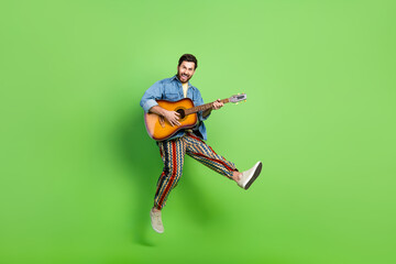 Full length photo of excited positive guy dressed jeans shirt jumping high enjoying guitar music...