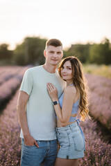 Male embracing female enjoying romantic time in sunset. Young couple kissing together in purple lavender field. Beautiful woman hugs man among violet flowers with sunlight on summer day.