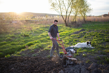 organic farming man ploughs the ground at sunset with a tiller preparing the soil for sowing