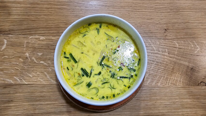 A bowl of curry coconut soup on a table made of wood, with fine herbs as ingredients Hanover Germany
