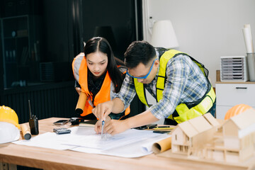 Engineer teams meeting working together wear worker helmets hardhat with on architectural project site and making model house. Asian industry professional team