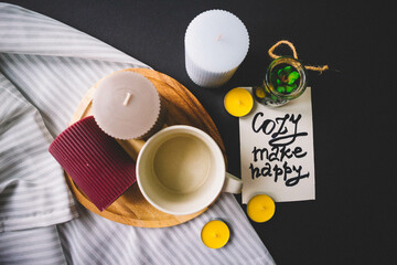 Candles, wooden board, cup, textile and cactus on a black background. Copy space