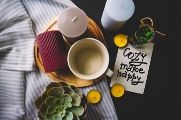 Candles, wooden board, cup, textile and cactus on a black background. Copy space