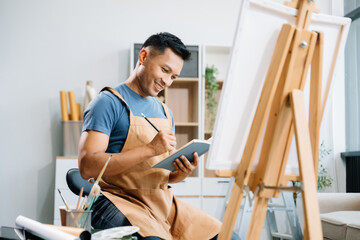 Asian male painter do artwork in art workshop, painting supplies, oil pastels, two canvas easel,...