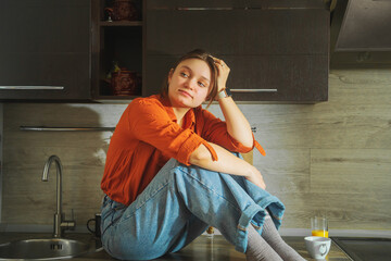 Beautiful young woman sitting on the kitchen countertop.