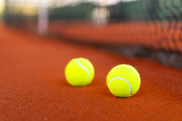 tennis balls on orange clay court with blurred net in background