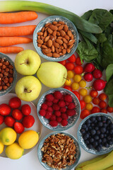 Apples, lemons, bananas, berries, carrots, leek, tomatoes, radishes, spinach and various nuts on white background. Healthy seasonal fruit and vegetable. Top view.