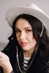 Portrait of eautiful brunette makeup artist in white trousers, black leather jacket and white hat...