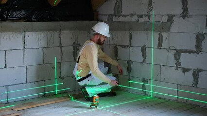 Builder using laser level in building on construction site. Construction worker installing and adjusting laser level on floor before measuring - Powered by Adobe
