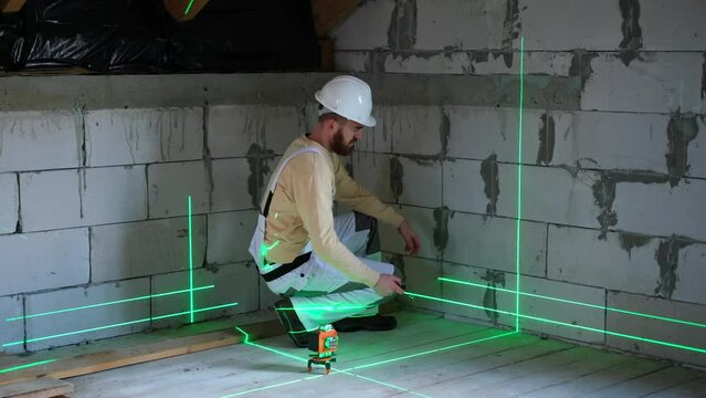 Builder using laser level in building on construction site. Construction worker installing and adjusting laser level on floor before measuring