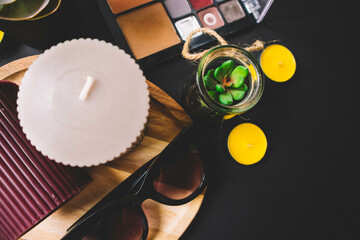 Candles, wooden board, shadow, cactus, makeup brushes and sunglasses on a black background. Copy...