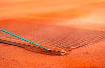 tennis player drag brushing the orange clay to maintenance clay court surface
