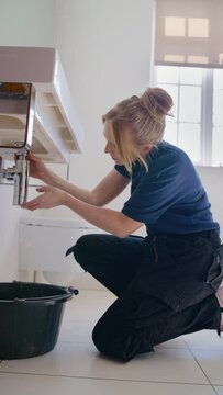 Vertical video of female plumber fixing leak in domestic bathroom sink  - shot in slow motion
