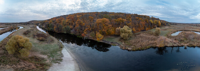 Aerial wide panorama of river valley with golden autumn forest and grey cloudy sky in Ukraine countryside