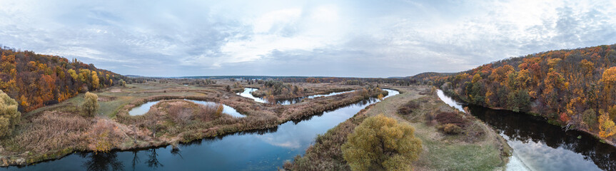 Aerial trees growing on river curve panorama with autumn forest and scenic cloudy sky in Ukraine