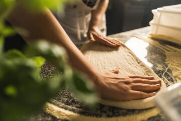 hands stretching pizza dough on floured surface. Expert touch in traditional Italian pizza making...
