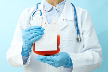 Doctor with bag with donor blood in hands on blue background, close up