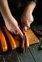 Slicing smoked sausages on a kitchen board. The chef hands cut sausage with a knife before...