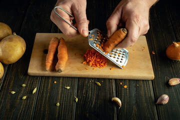 Close-up of a chef hands grating carrots on a kitchen board before preparing a vegetarian breakfast...