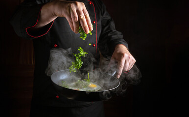 A chef in uniform throws fresh parsley into a frying pan with eggs. Space for advertising on a...