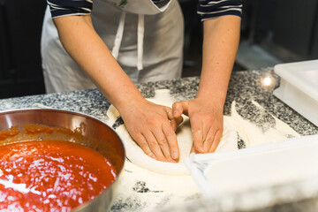 closeup shot of hands stretching the dough for pizza, tomato sauce on the table. High quality photo