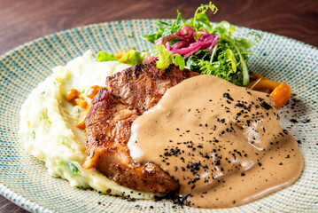 Delicious grilled steak served with pepper sauce, mashed potatoes, and fresh salad on a textured plate, showcasing vibrant colors and textures.
