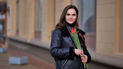 Portrait of a happy brunette girl with a tulip in the background of the city in the cold season.