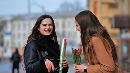 two happy girls, students, friends with flowers in their hands, laughing