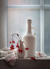 Still life with a white bottle and viburnum in a vase on the windowsill