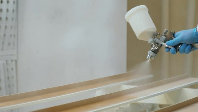 carpenter spray painting wood piece while working in joinery workshop. High quality 4k footage
