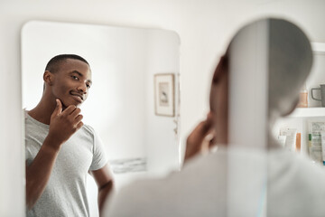 Smiling African man looking at his face in a bathroom mirror