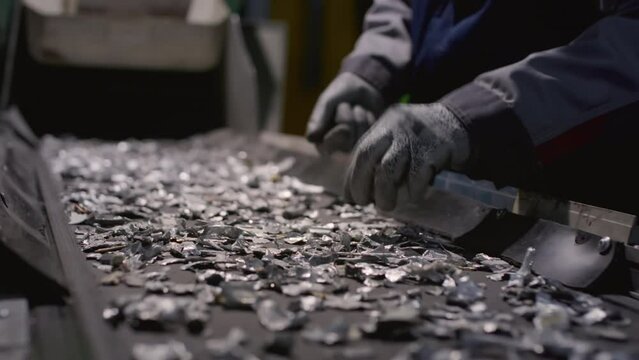 Man sorts pieces of non-ferrous metal, iron or steel on a conveyor belt with his hands or palm. Male chooses aluminum chips for recycling and remelting. Garbage factory or waste plant.