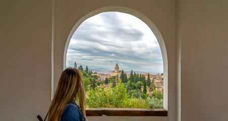Rear view of young woman traveler looking at the Alhambra complex from Generalife, Granada, Spain.