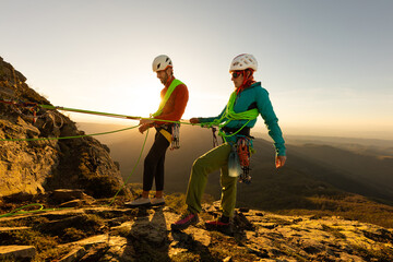 Two people are climbing a mountain, one of them is wearing a green harness. The other person is...