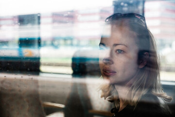 Woman traveler contemplating outdoor view from window of train. Young lady on commute travel to work sitting in bus or train