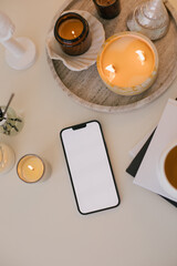 Fototapeta premium Smartphone with white empty display on a white table with candles, aromatic sticks and home decor.