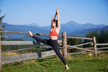 Woman practicing yoga outdoors in the mountains in a serene, natural setting. Female performing yoga pose, with backdrop of beautiful mountain landscape at sunrise or sunset.