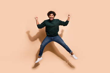 Fototapeta na wymiar Full body portrait of nice young man jump raise fists wear sweater isolated on beige color background