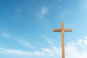 A simple wooden cross standing alone against a clear blue sky, symbolizing faith and spirituality, with space for text on the sky background