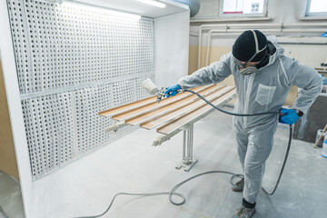 worker with safety mask painting a piece of wood with spray gun in home workshop. High quality photo